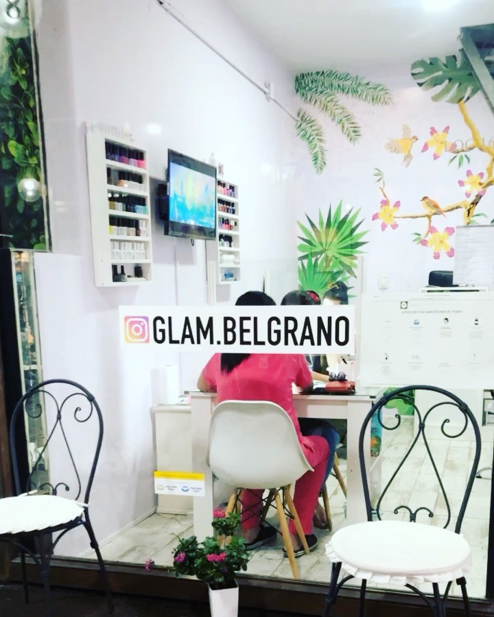 El salón de GlamB visto a través de la vidriera: estanterías de esmaltes, el televisor y el mural tropical sobre las paredes lila